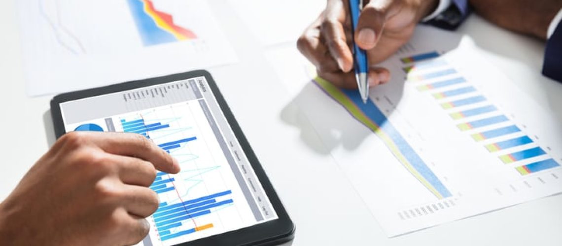 Close-up Of Two Businesspeople Using Digital Tablet While Working On Graph On Desk At Workplace